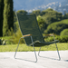 A green outdoor lounge chair with bamboo armrest placed on an outdoor area near grassy field