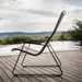 A black outdoor lounge chair with bamboo armrest placed on a wooden deck beside the pool