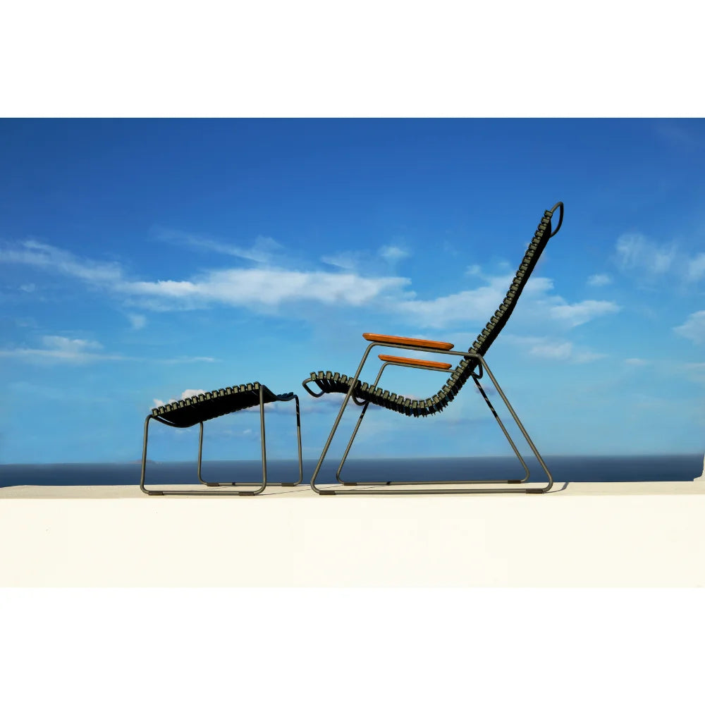 A dark green outdoor lounge chair with bamboo armrest and dark green outdoor footrest on a white surface under a blue sky