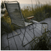 A green outdoor lounge chair with bamboo armrest and an outdoor footrest placed on a wooden deck surrounded by tall grass