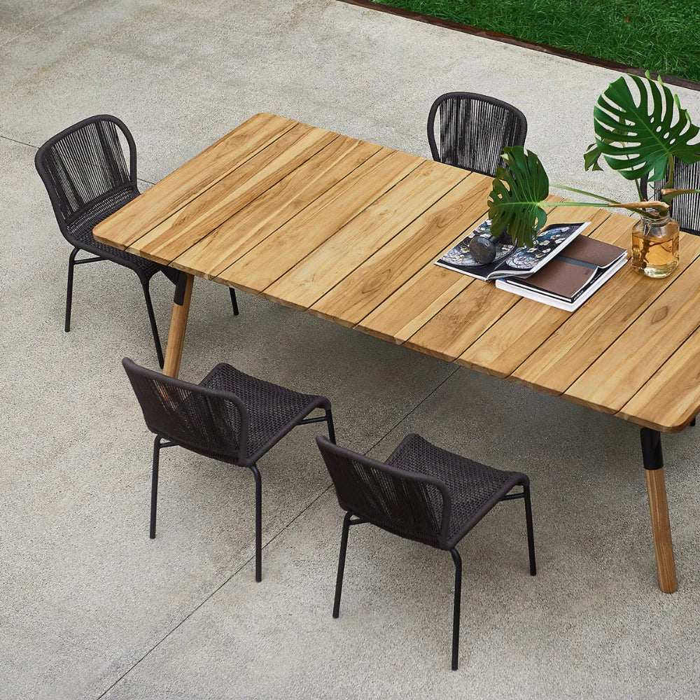 Five black wicker outdoor chair placed around wooden rectangular table set on an outdoor patio