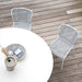 Two white wicker outdoor chair beside white round dining table on a wooden deck patio