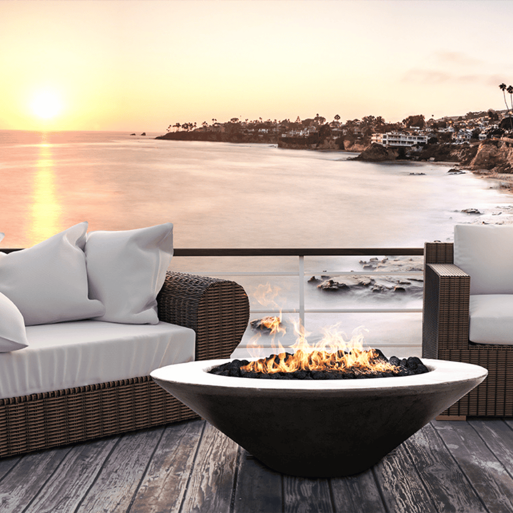 Grey outdoor round concrete fire bowl with sofa and chair set on a wooden deck outdoor setting with a serene view of coastal landscape