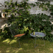 A gray round outdoor tray table and an outdoor lounge chair placed on a lawn area surrounded by plants