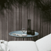 A gray round outdoor tray table with black carafe matching black glass on top placed against wooden fence