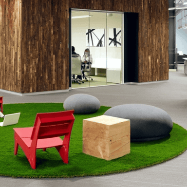 Grey fabric wrapped pebble seat on an artificial grass carpet in an office space, accompanied by red chair and wooden box