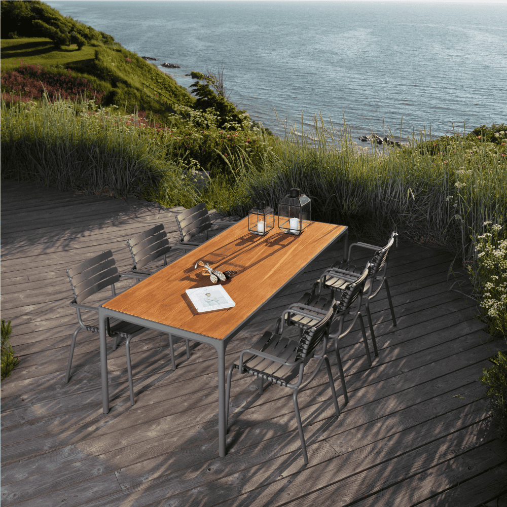 A rectangular wooden outdoor dining table with gray aluminum frame and 6 gray dining chairs set on a wooden deck patio