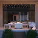  White round hidden propane tank fire pit placed on a modern patio with sectional sofa beside glass wall and string lights