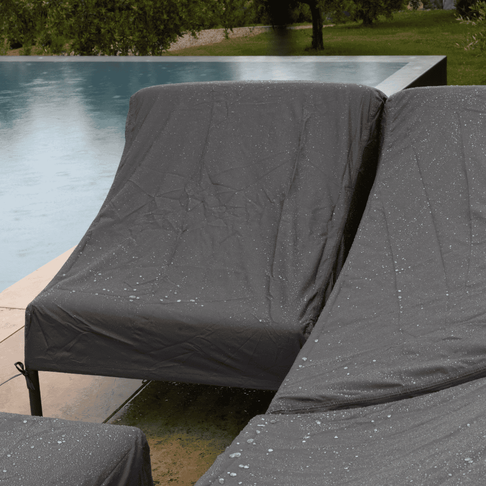 A sofa and chairs beside the pool covered by dark gray patio seat covers