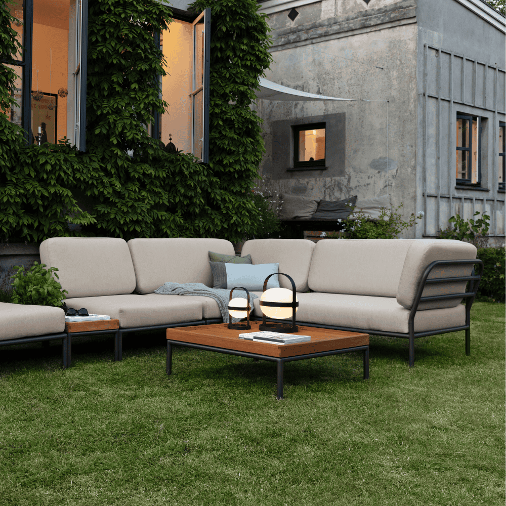 A lawn surface patio with square wooden outdoor coffee table with black aluminum frame and beige outdoor sectional sofa