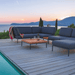 A wooden deck poolside with square wooden outdoor coffee table with gray aluminum frame and dark gray sectional sofa