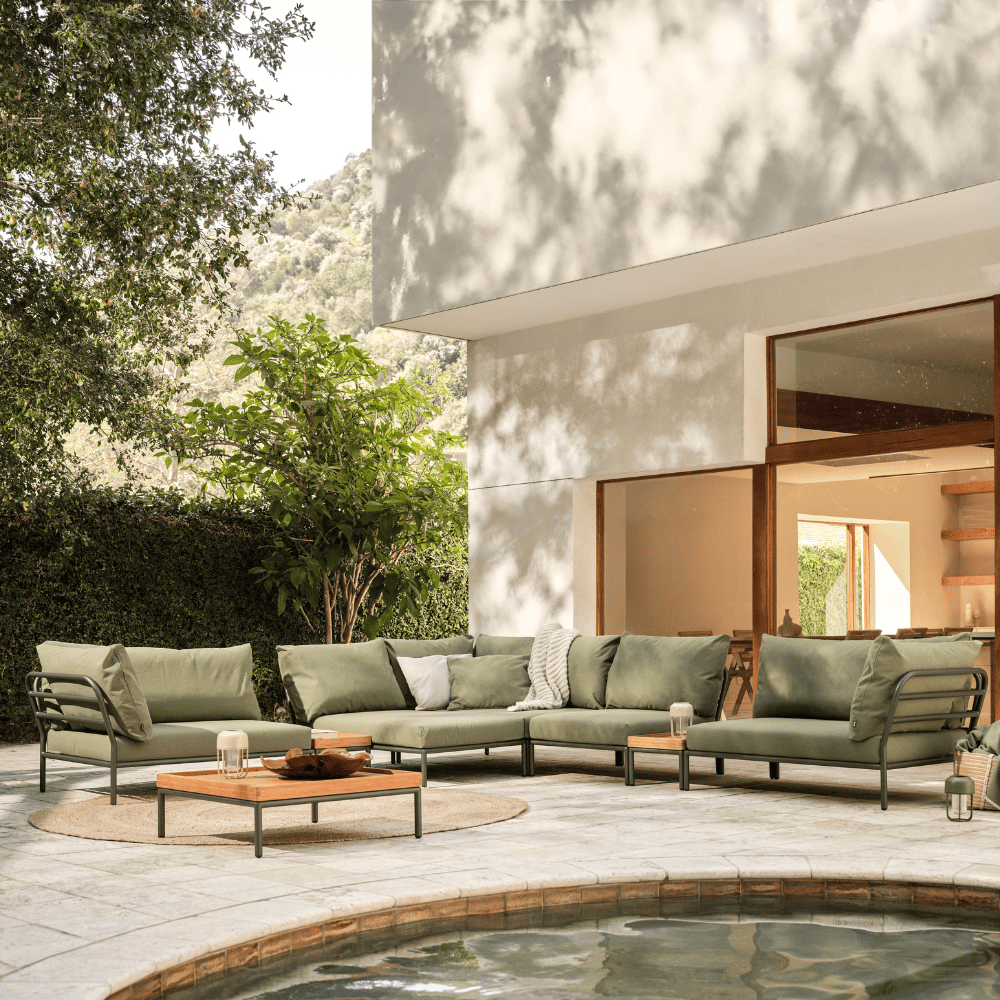 A patio seating area with square wooden outdoor coffee table with gray aluminum frame and green outdoor sectional sofa