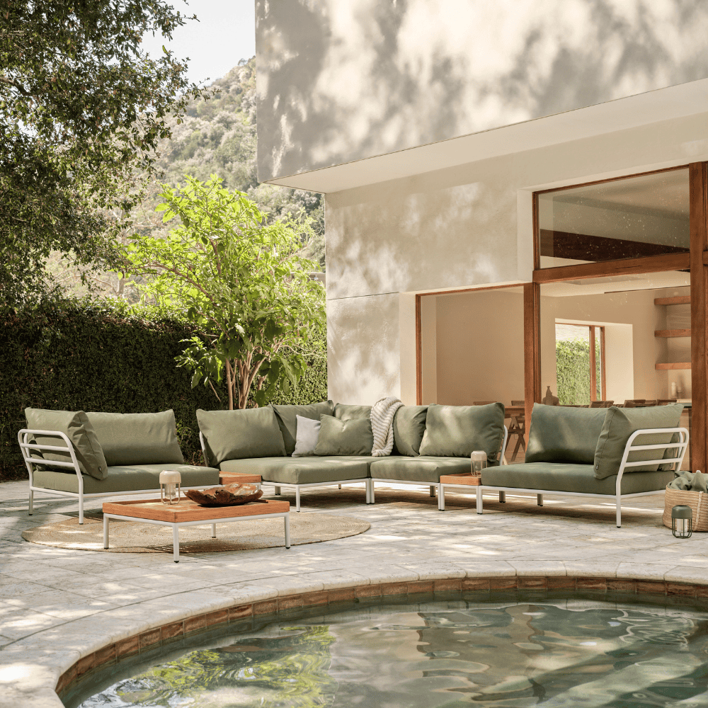 Green outdoor sectional sofa with white aluminum frame and square wooden outdoor coffee table set on a patio near the pool