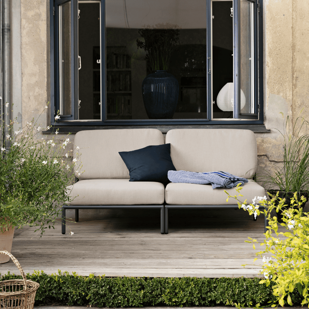 2 beige outdoor lounge chairs with gray aluminum frame placed on a wooden deck in front of a large window