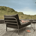 A dark gray outdoor lounge chair with gray aluminum frame and a black outdoor tray table set on a wooden deck near grassy area