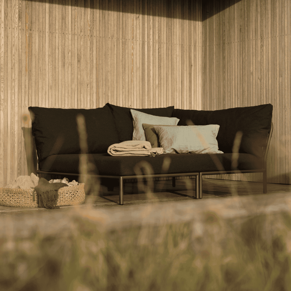 A black right corner lounge sofa with black aluminum frame placed on a wooden deck patio against wooden wall