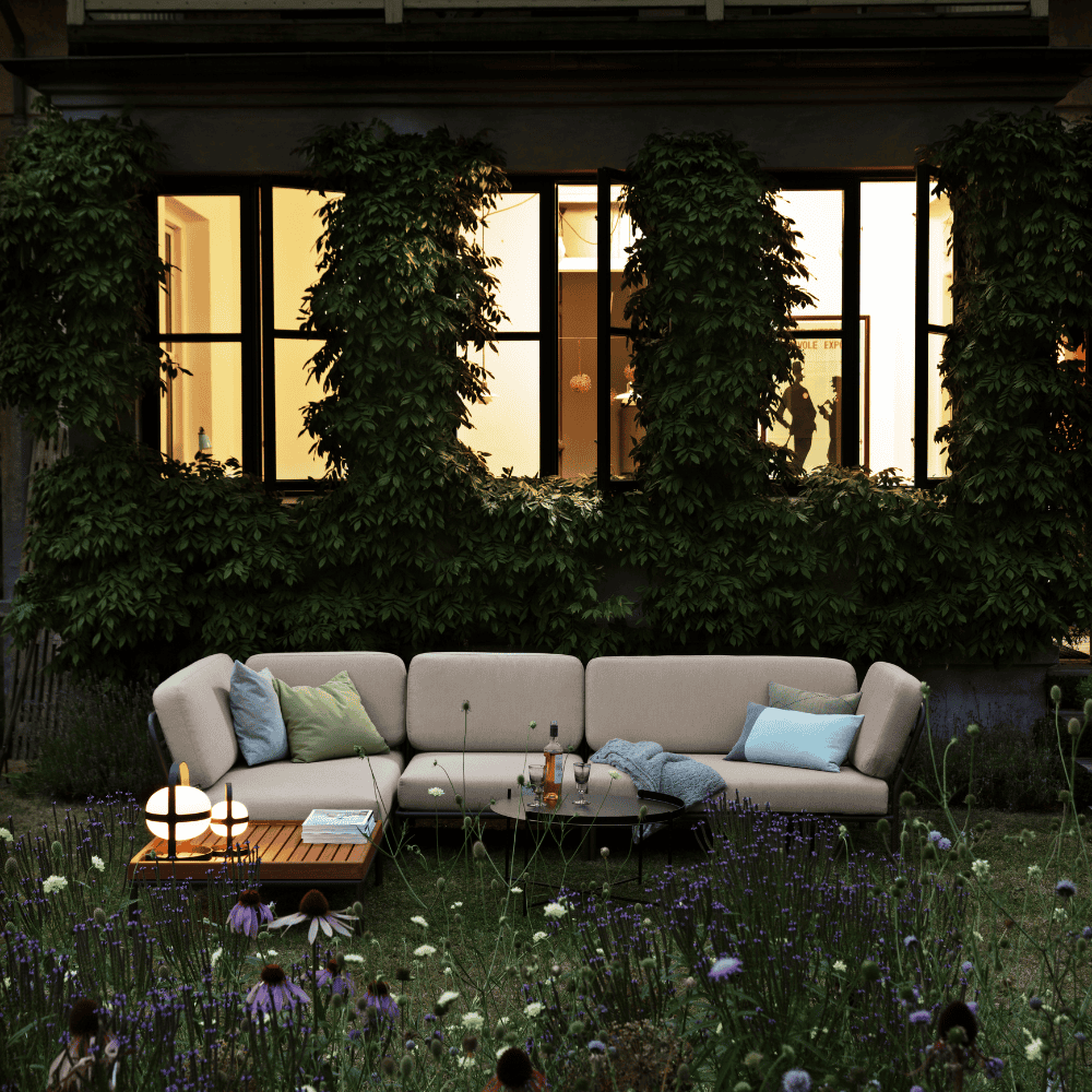 Beige outdoor sectional sofa, wooden outdoor coffee table and outdoor tray table set on a patio surrounded by greenery