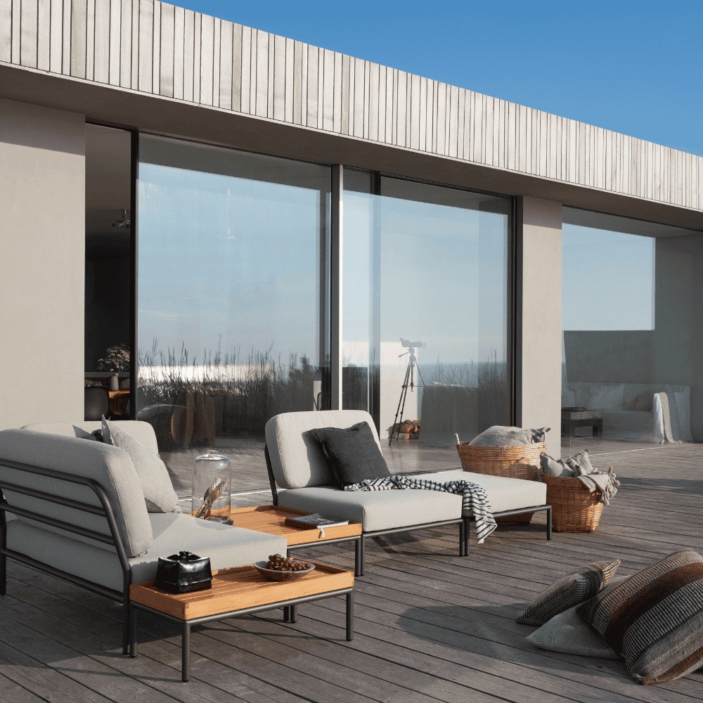 A wooden outdoor side table, square wooden outdoor coffee table and beige outdoor sectional sofa set on a wooden deck patio