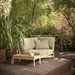 A rectangular wooden outdoor side table with light green right corner lounge sofa set on a wooden deck patio with greenery