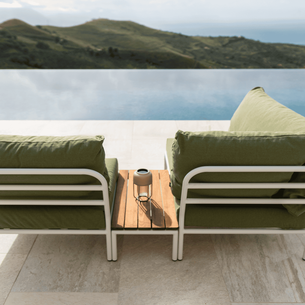 A rectangular wooden outdoor side table and green outdoor lounge chair and corner sofa with white aluminum frame set beside the pool