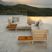 A beige outdoor sectional sofa and wooden outdoor coffee table and rectangular outdoor side table set beside the pool