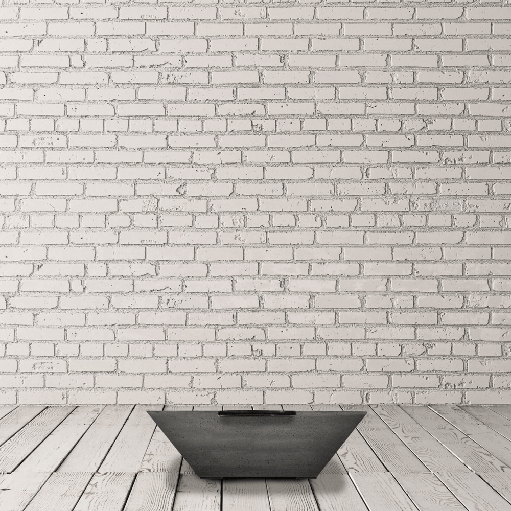 Small tapered shaped square concrete fire water bowl placed on a wooden deck against white brick wall