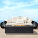  An outdoor setting featuring a dark gray outdoor concrete rectangular fire pit in front of a black modern wicker sofa with white cushions and pillows