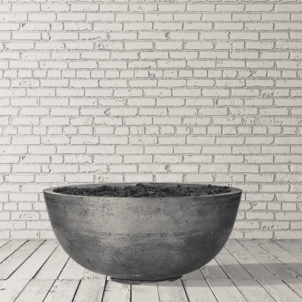 Grey round outdoor concrete fire bowl placed on a wooden deck against white brick wall