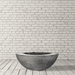 Grey round outdoor concrete fire bowl placed on a wooden deck against white brick wall