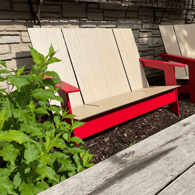 Red outdoor lounge bench with light brown wood grain seat and backrest placed against stone wall beside green plants