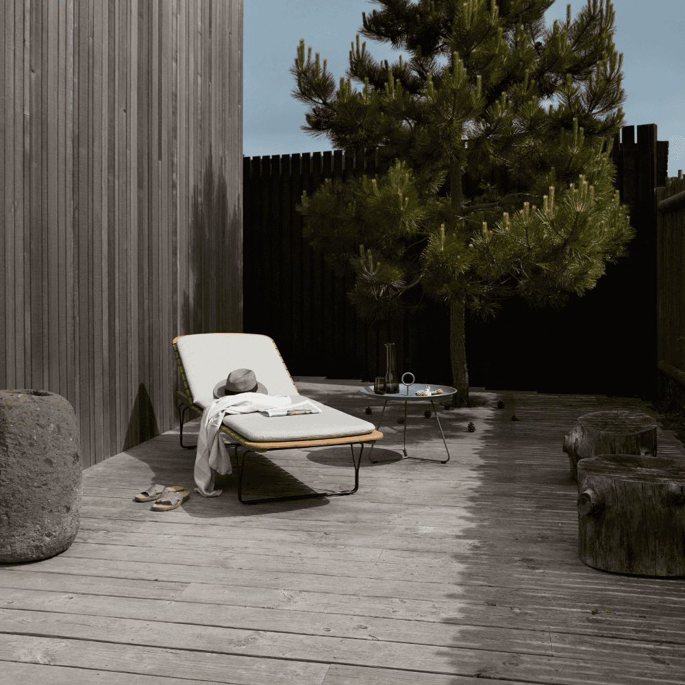 A bamboo lamellas outdoor sunbed with light gray sunbed cushion placed on a wooden deck patio near the tree