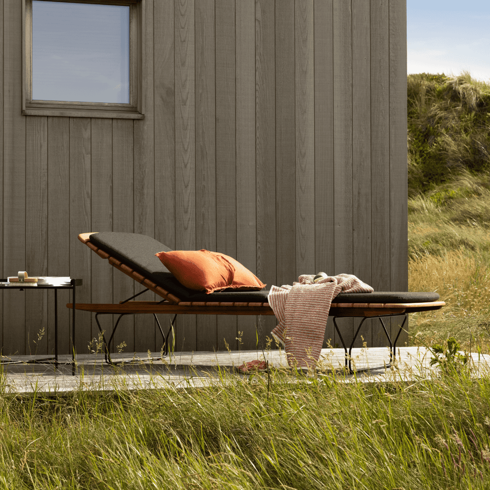 A bamboo lamellas outdoor sunbed with black sunbed cushion set on a wooden deck patio beside gassy area