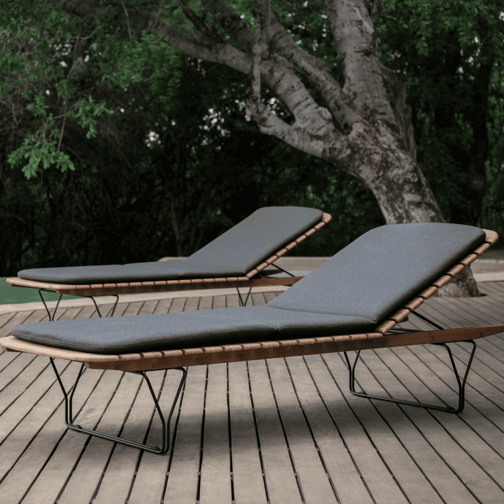 2 bamboo lamellas outdoor sunbed with dark gray sunbed cushion placed on a wooden deck beside the pool with a large tree