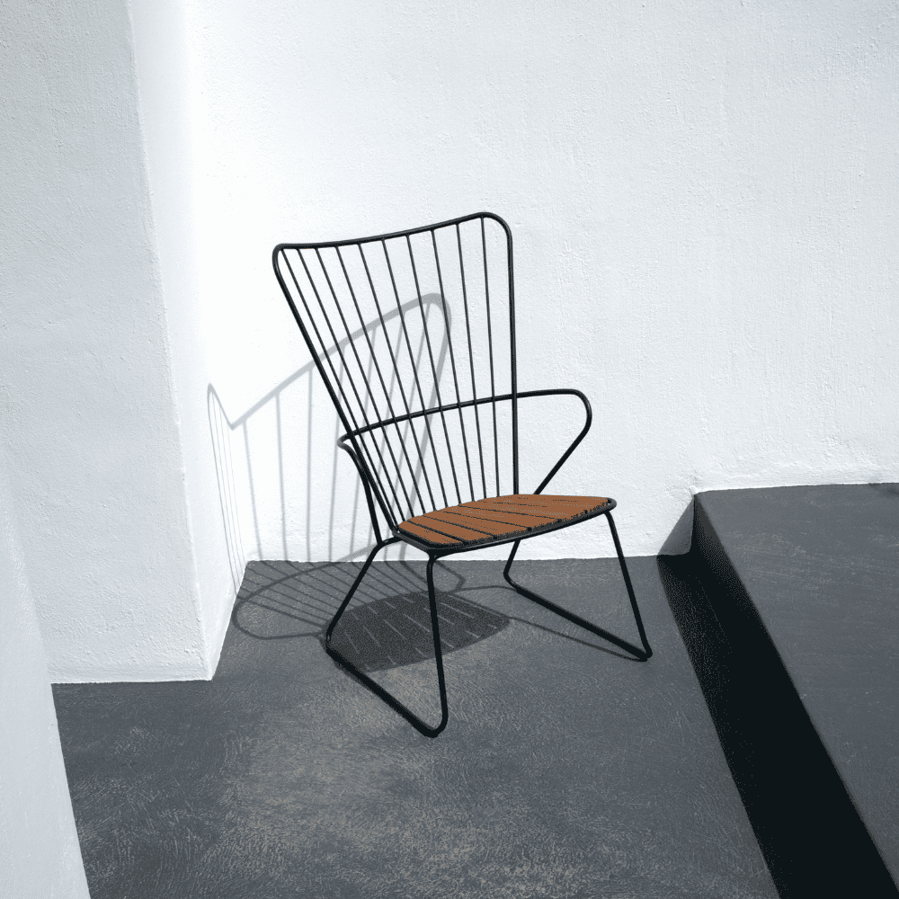 A black metal outdoor lounge chair with bamboo lamellas seat placed against white wall