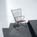 A black metal outdoor lounge chair with bamboo lamellas seat placed against white wall