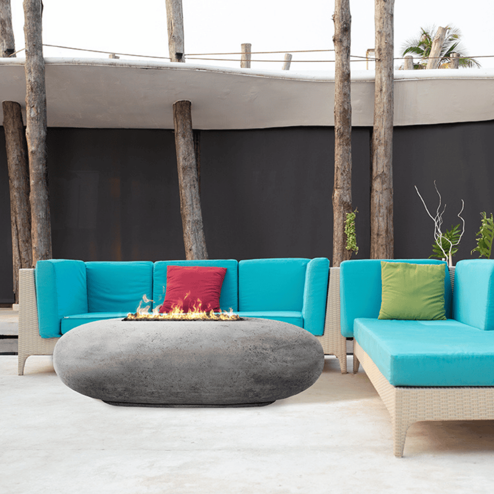 Grey pebble outdoor concrete oval fire table sets on an outdoor patio area accompanied by two light blue sofas