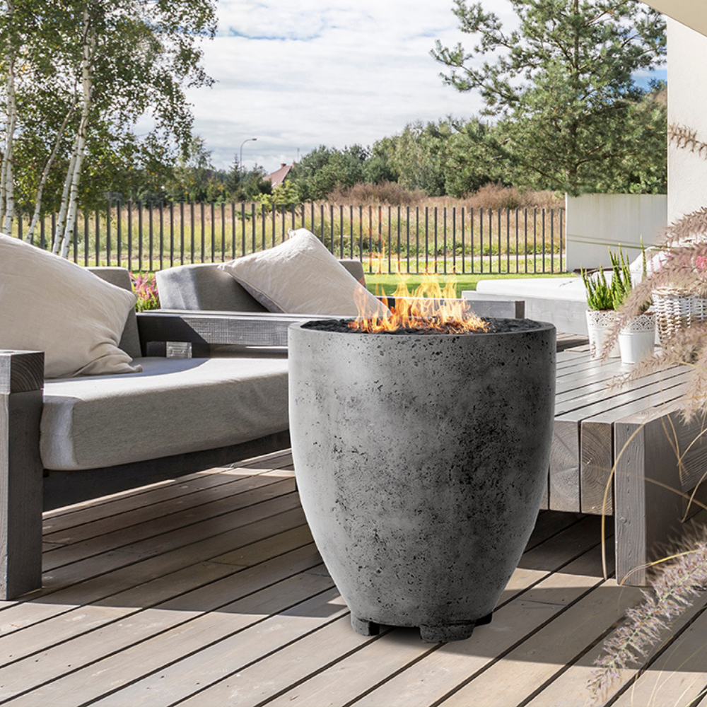 A wooden deck outdoor patio featuring a grey outdoor concrete fire bowl beside wooden table and wooden chairs with cushions