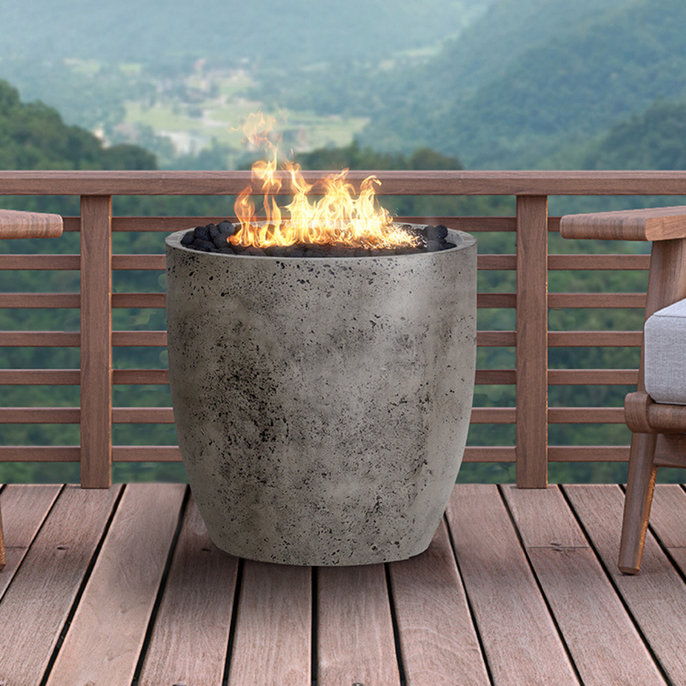 A grey round outdoor concrete fire bowl placed on a wooden deck balcony with view of green mountain landscape