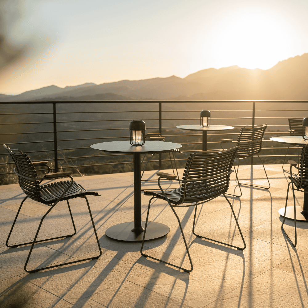 Several black round outdoor coffee tables and black outdoor dining chairs set on a terrace with view of a distant mountains