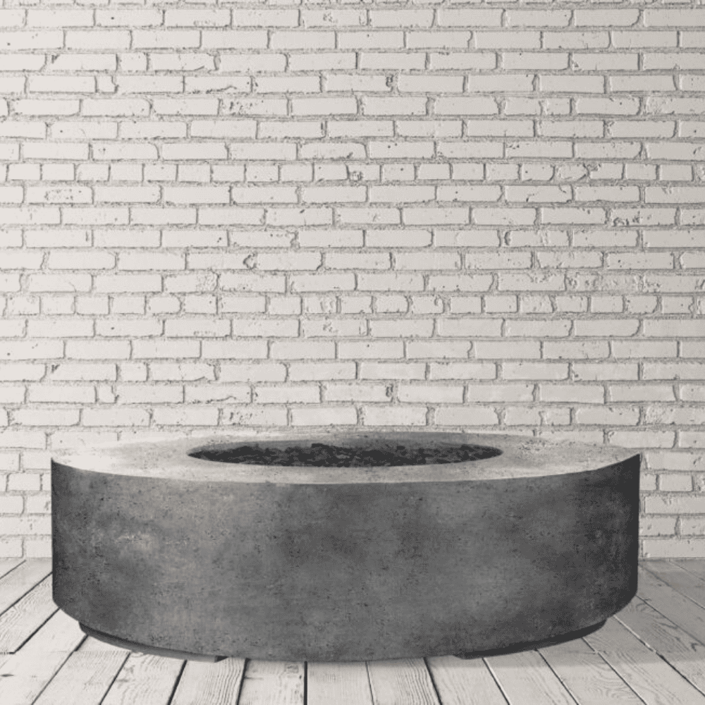 Grey outdoor round concrete fire pit table with lava rocks placed on a wooden deck against white brick wall