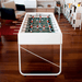 A white outdoor football table with wooden handles situated on a wooden floor in an indoor space