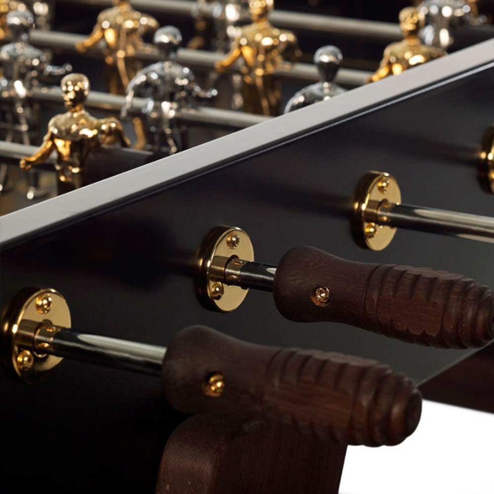 Close-up view of a black outdoor football table focusing on wooden handles attached to a gold bracket and gold and silver colored players