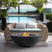 A dark gray concrete large outdoor fire pit bowl set in a modern outdoor seating area in front of brown woven sofa with cushion 
