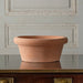 An empty round low bowl  Italian Terra Cotta Pot placed on a wooden surface against paneled wall
