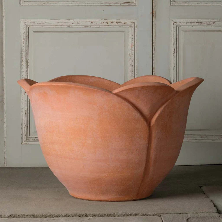 A large Italian Terra Cotta outdoor planter for patio with a tulip-like design placed on a stone wall against paneled wall