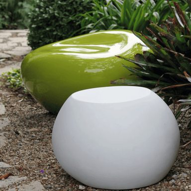 White concrete pebble garden table and green concrete pebble garden seat on a gravel surface in a garden area beside plants