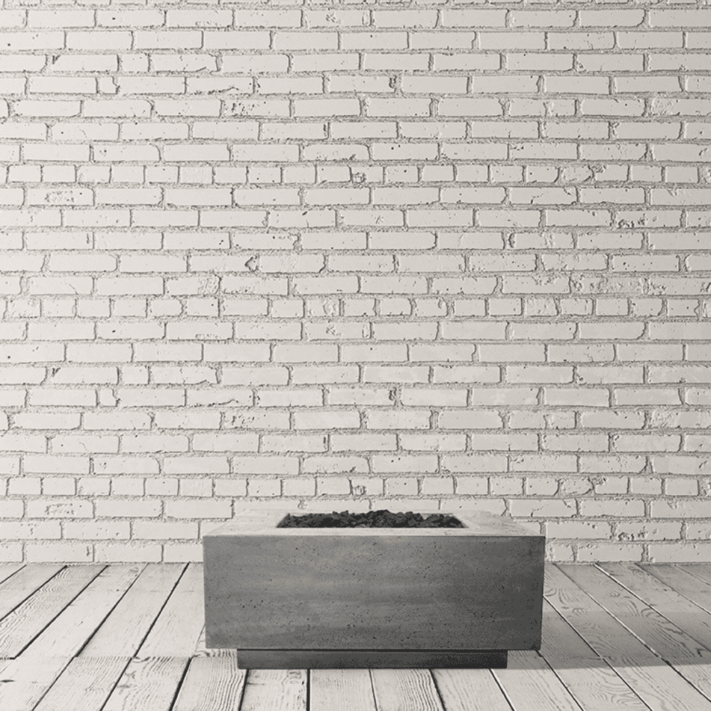 A grey square outdoor concrete fire table with lava rocks placed on a wooden deck with white brick wall