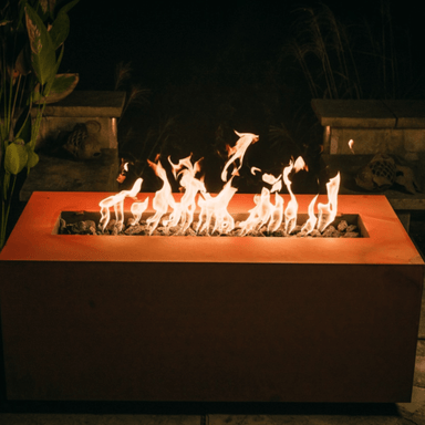 Orange rectangular powder coated metal fire pit with vibrant flames situated on a patio at night beside plants