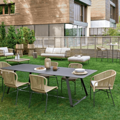 Six light brown outdoor wicker armchairs set around black rectangular dining table on a grassy area patio setting